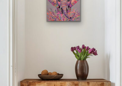 Buntes Neo-Pop-Art Kunstwerk eines Elefanten an einer weißen Wand über einem rustikalen Holztisch mit einer Vase voller lila Tulpen.