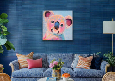 Buntes Koala-Gemälde im Pop-Art-Stil an einer tiefblauen, strukturierten Wand über einem gemütlichen blauen Sofa mit dekorativen Kissen.