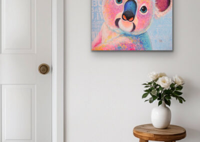 Buntes Koala-Gemälde im Pop-Art-Stil an einer weißen Wand neben einer geschlossenen Tür über einem rustikalen Holzhocker mit weißen Rosen.