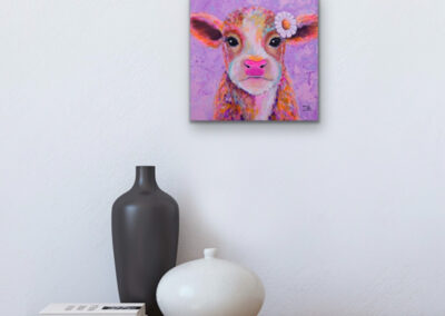 Buntes Tierportrait eines kleinen Kalbs im Pop-Art-Stil an einer hellen Wand über einer Holzablage mit einer schwarzen und einer weißen Design-Vase.