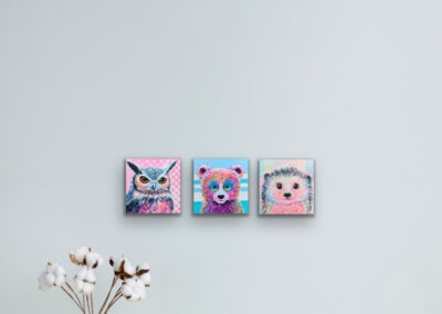 Drei kleine, quadratische Pop-Art-Tierbilder nebeneinander an einer hellgrauen Wand über einer Bodenvase mit weißen Baumwollzweigen.