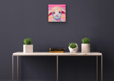 Quadratisches, buntes Lamm-Gemälde im Pop-Art-Stil an einer dunkelgrauen Wand über einem minimalistischen Konsolentisch mit drei kleinen Zimmerpflanzen.