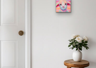 Quadratisches, farbenfrohes Lamm-Gemälde an einer weißen Wand neben einer geschlossenen Tür und über einem Holzhocker mit weißen Blumen.