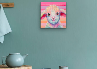 Farbenfrohes Kunstwerk eines Lamms im Pop-Art-Stil an einer salbeigrünen Wand über einem Holztisch mit einer blauen Teekanne und Bechern.