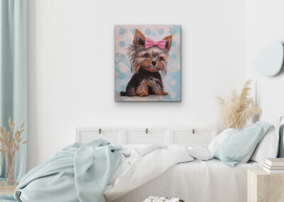 Pop-Art-Portrait eines kleinen Hundes mit rosa Schleife an einer weißen Wand in einem hellen Schlafzimmer über einem Bett mit hellblauer Decke.