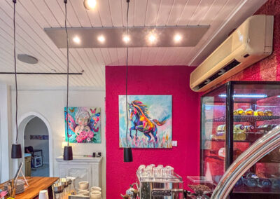 Farbenfrohe Raumgestaltung für die Gastronomie: Moderne Tierporträts im Neo-Pop-Art-Stil von Silke Timpe (Pferd und Löwe) setzen energetische Akzente an einer intensiv pinken Wand hinter einer Theke.