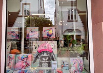 Schaufenstergestaltung mit moderner Kunst: Farbenfrohe Tierporträts von Silke Timpe im Neo-Pop-Art-Stil mit urbanen Einflüssen ziehen die Blicke im Außenbereich auf sich.