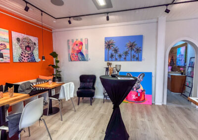 Inspiration für gewerbliche Räume: Moderne, farbenfrohe Kunstausstellung von Silke Timpe in einem stilvollen Café mit Stehtischen, orangen Akzentwänden und ausdrucksstarken Tierporträts.