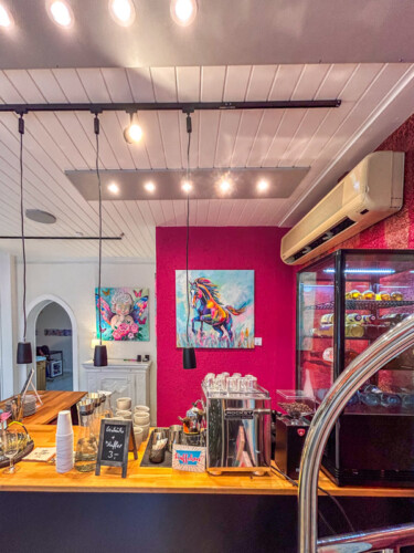 Farbenfrohe Raumgestaltung für die Gastronomie: Moderne Tierporträts im Neo-Pop-Art-Stil von Silke Timpe (Pferd und Löwe) setzen energetische Akzente an einer intensiv pinken Wand hinter einer Theke.