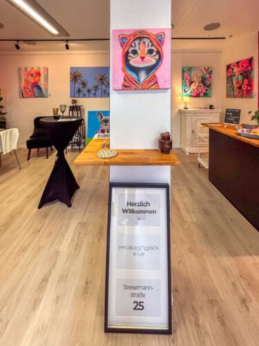 Stilvolle Innenraumgestaltung mit Kunst: Ein farbintensives Katzen-Gemälde im Pop-Art-Stil von Silke Timpe ziert eine zentrale Säule über einem modernen Stehtisch aus Holz.