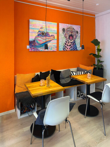 Wandgestaltung für ein Café oder Restaurant: Ein farbgewaltiges Krokodil- und ein Leopardengemälde im Neo-Pop-Art-Stil von Silke Timpe sorgen für ein inspirierendes Ambiente über den Tischen.