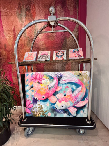 Kreative Kunstpräsentation: Farbgewaltiges Koi-Karpfen-Gemälde von Silke Timpe im Neo-Pop-Art-Stil mit pinken Fischen, dekorativ platziert auf einem silbernen Hotelgepäckwagen vor einer strukturierten Wand.