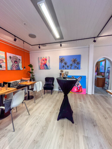 Inspiration für gewerbliche Räume: Moderne, farbenfrohe Kunstausstellung von Silke Timpe in einem stilvollen Café mit Stehtischen, orangen Akzentwänden und ausdrucksstarken Tierporträts.